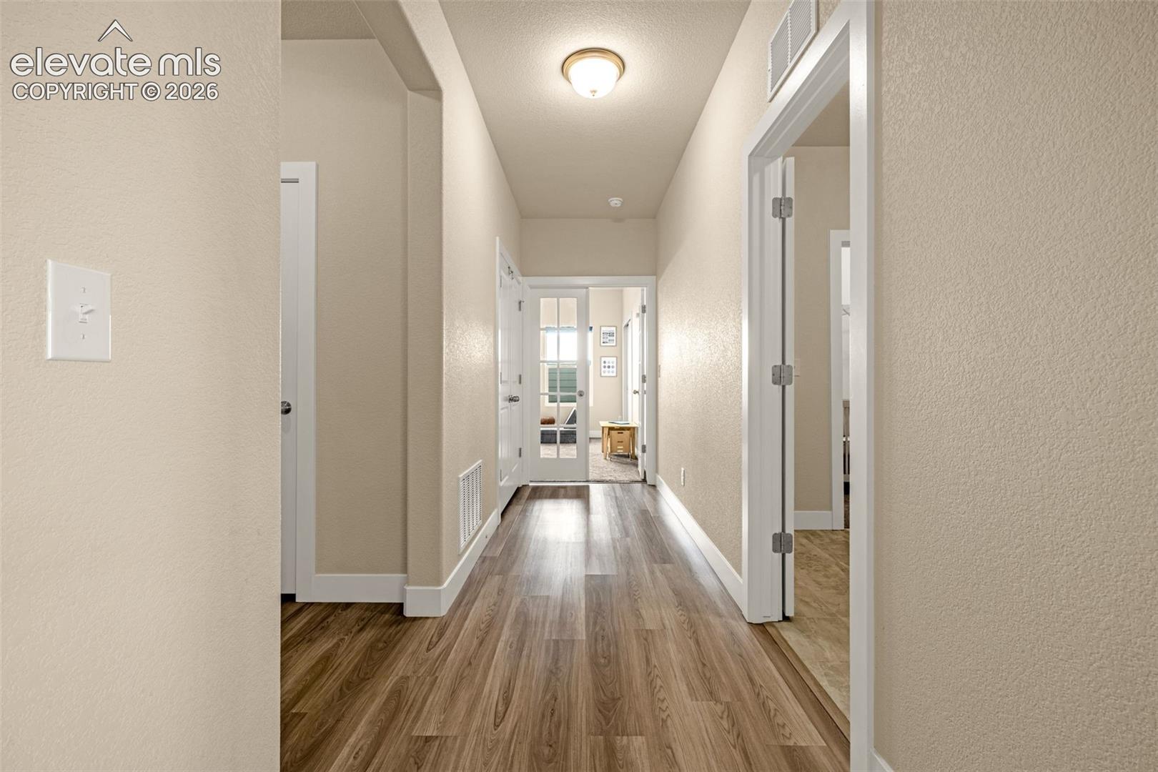 Long hallway with wood-look flooring, beige walls, white doors, and a view into a furnished room.