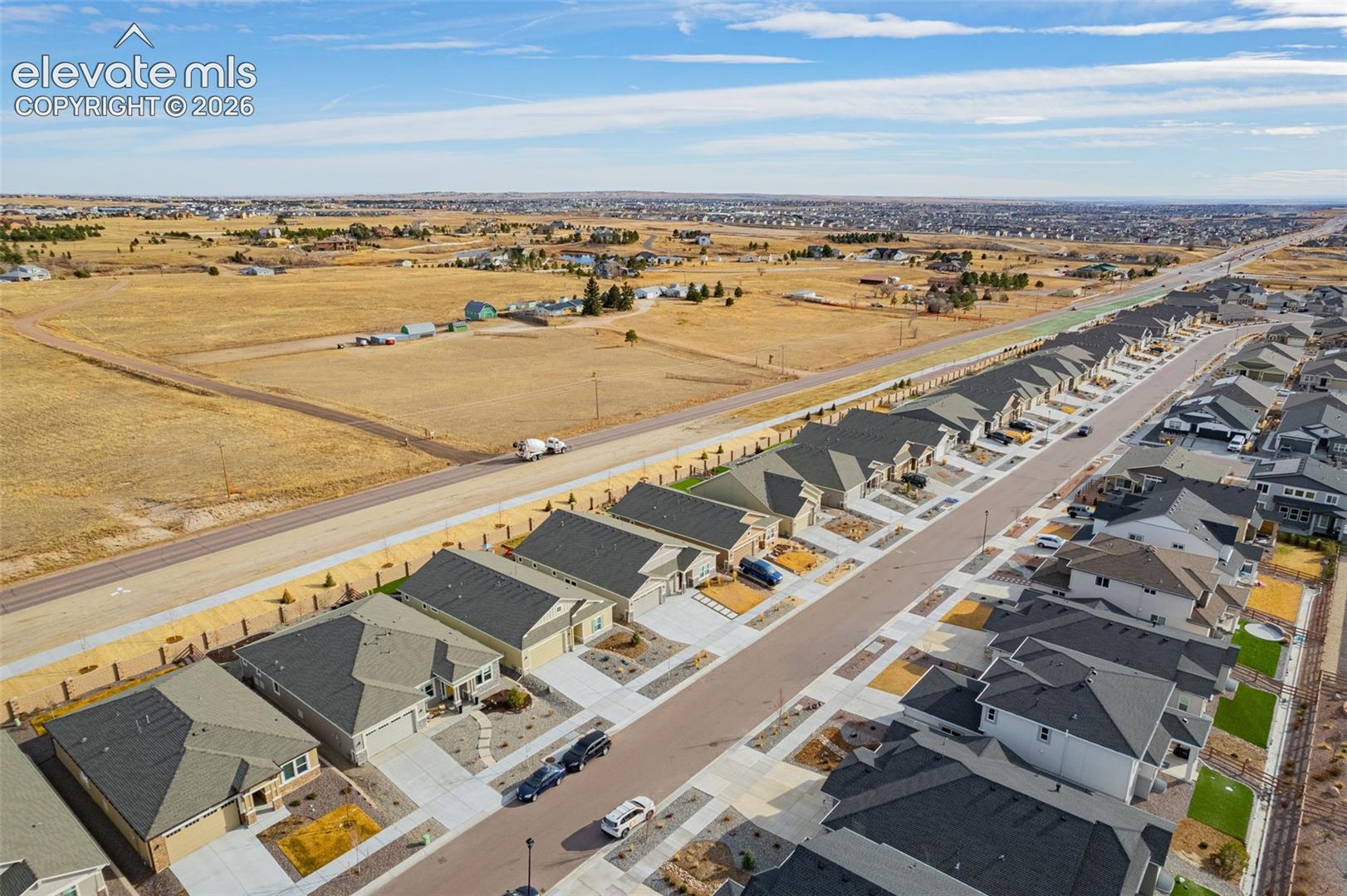 Aerial view of homes beside open fields, with dry grassland and development extending to the horizon.