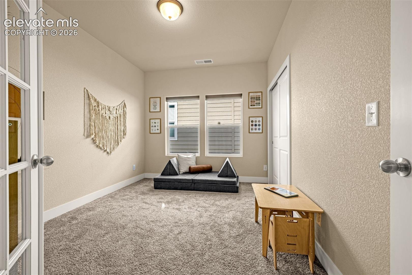 Furnished sitting room with a low dark sofa, plush carpet, and wooden desk.