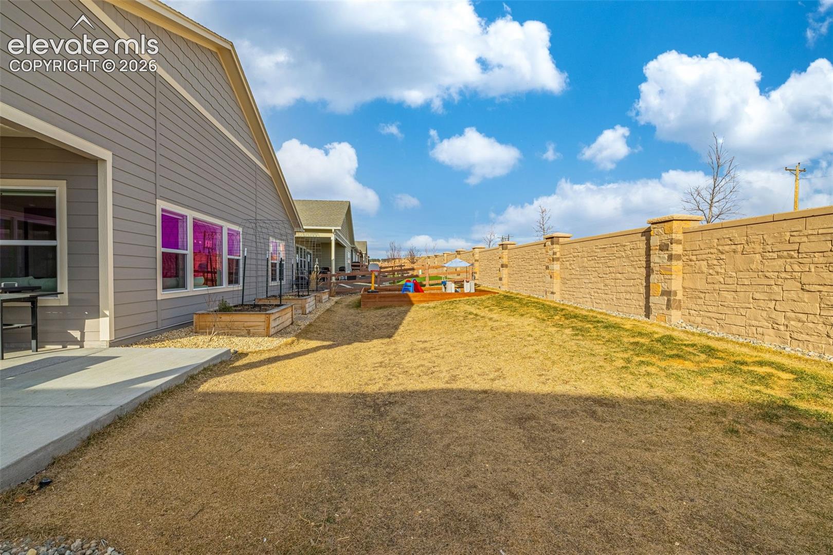 Backyard with raised garden beds, a small playset, and a tall stone privacy wall.