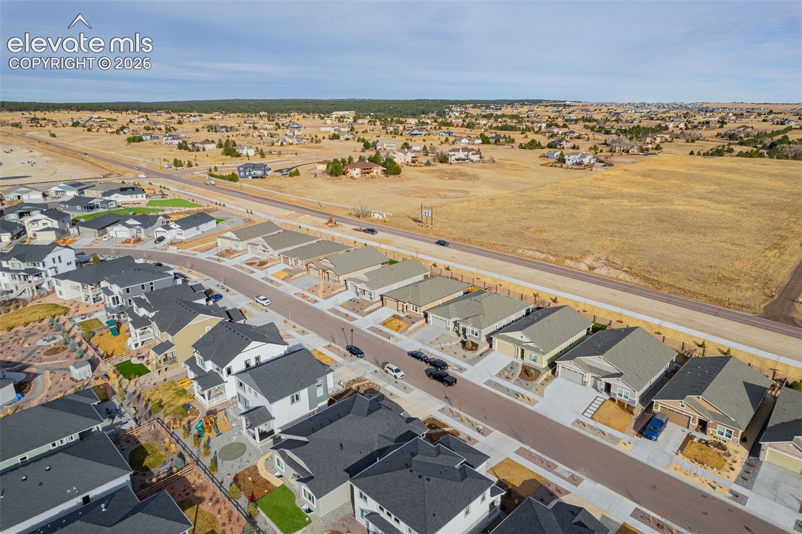 Aerial view of a residential neighborhood beside a large undeveloped field and main road.