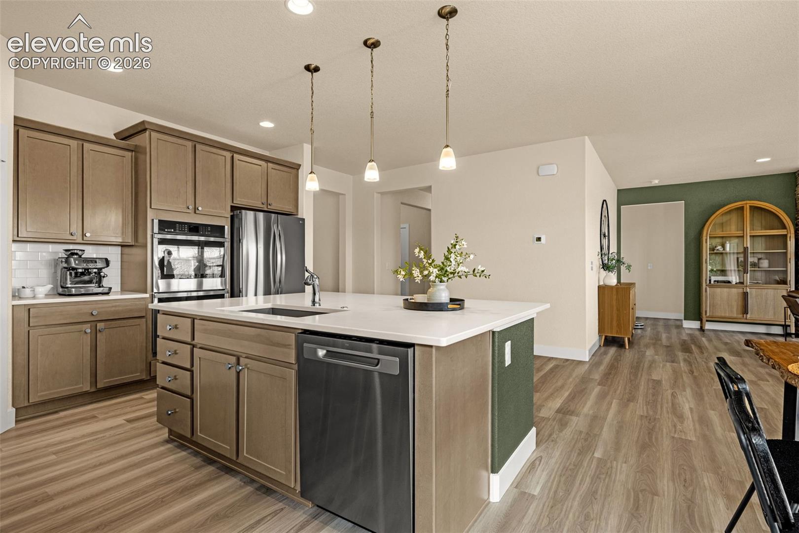 Open kitchen with a large white island, light wood cabinets, and stainless steel appliances.