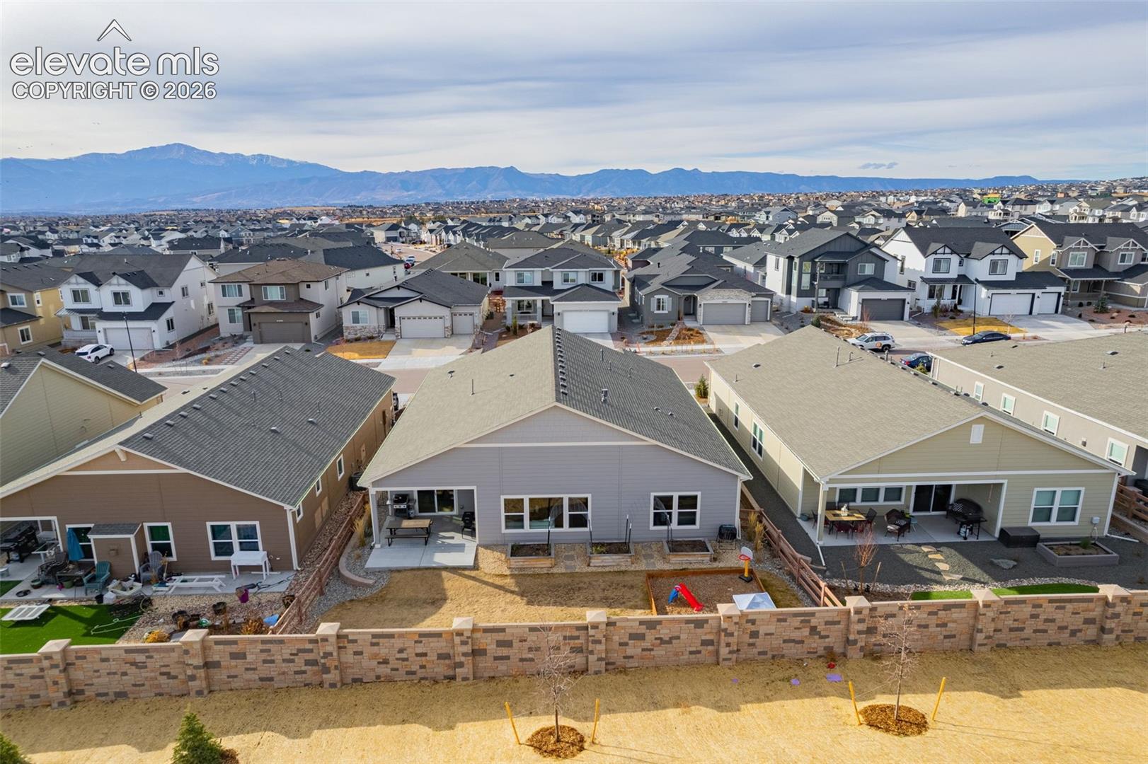 Aerial view of a fenced backyard and neighboring homes with mountains on the horizon.