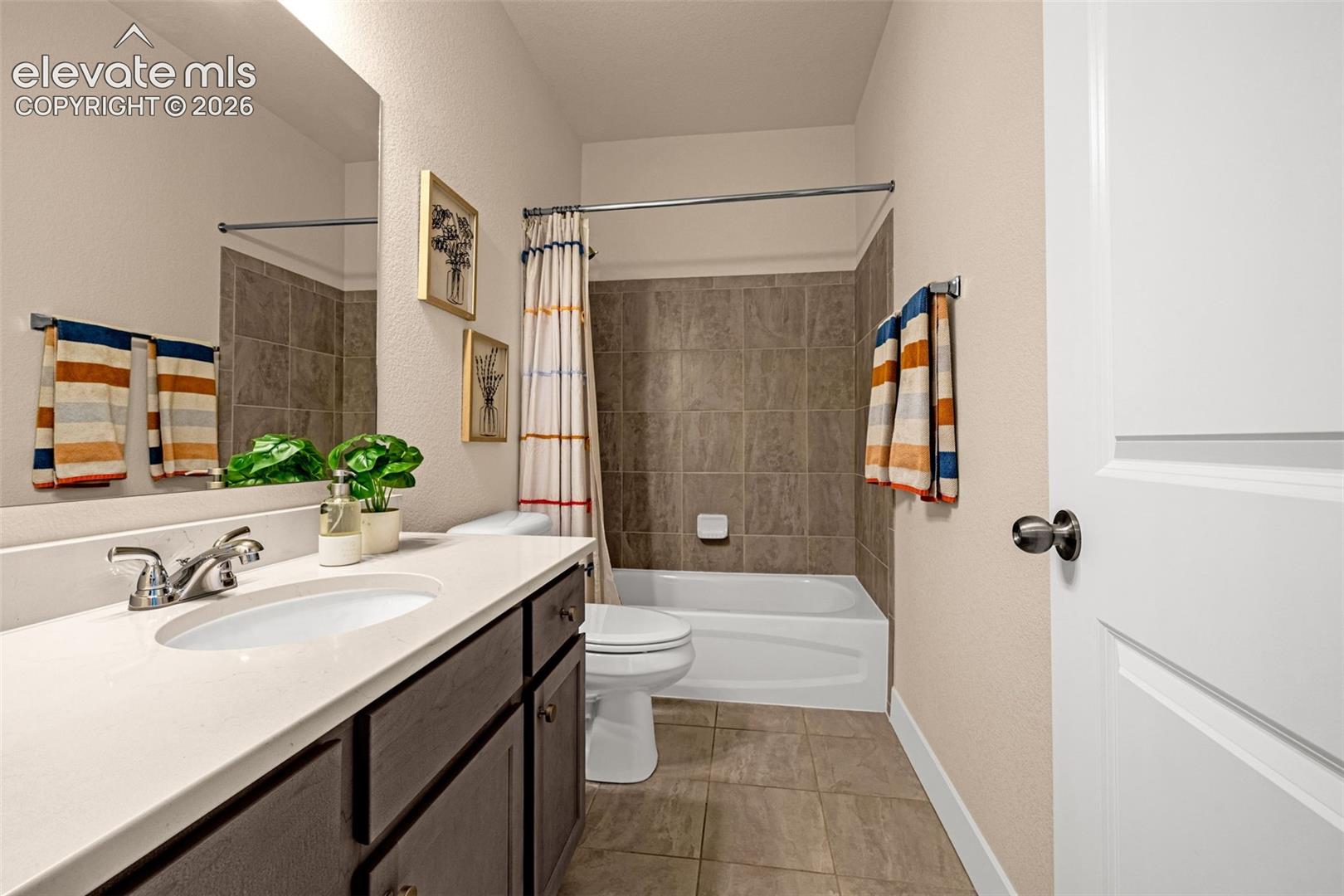 Bathroom with a white vanity, bathtub, gray-brown tile, and striped towels.