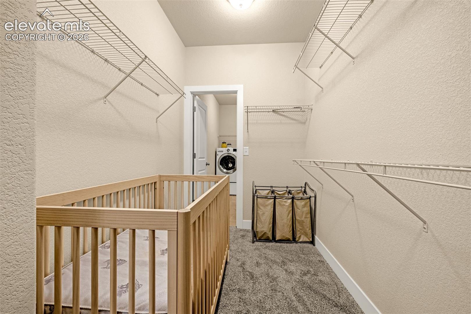 Walk-in closet with wire shelving, a wooden crib, and a laundry area through the doorway.