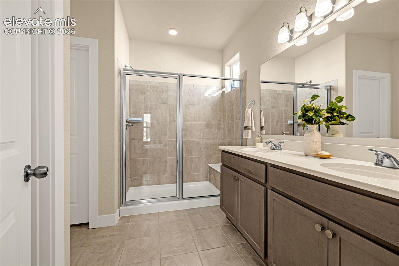 Bathroom with a glass-enclosed tiled shower and long double-sink vanity.