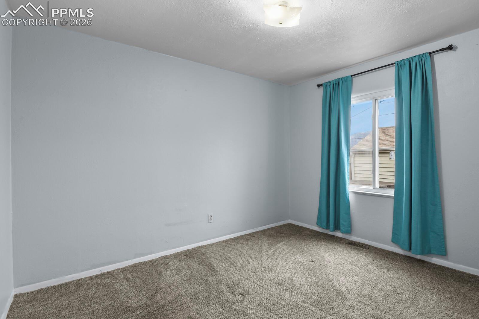 Vacant carpeted room with gray walls and a window framed by teal curtains.