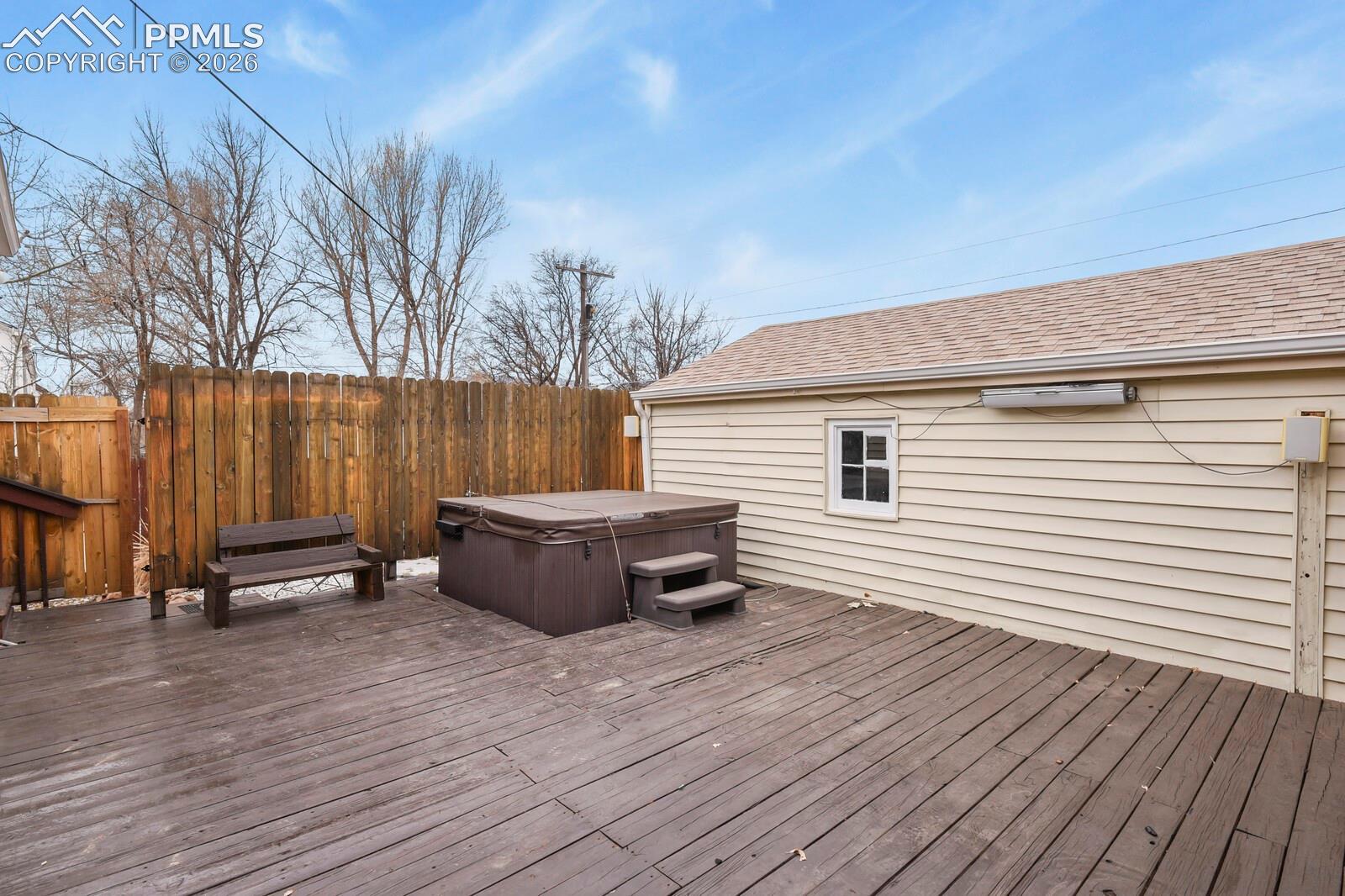 Backyard deck with a covered hot tub, steps, and bench beside the house.
