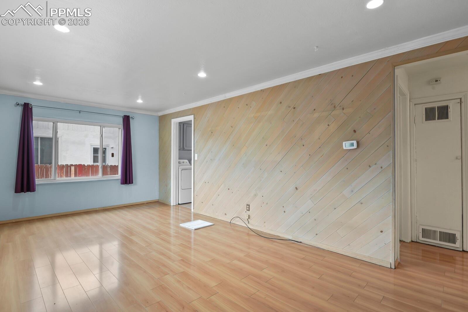 Vacant living room with diagonal wood paneling, light flooring, and a laundry doorway.