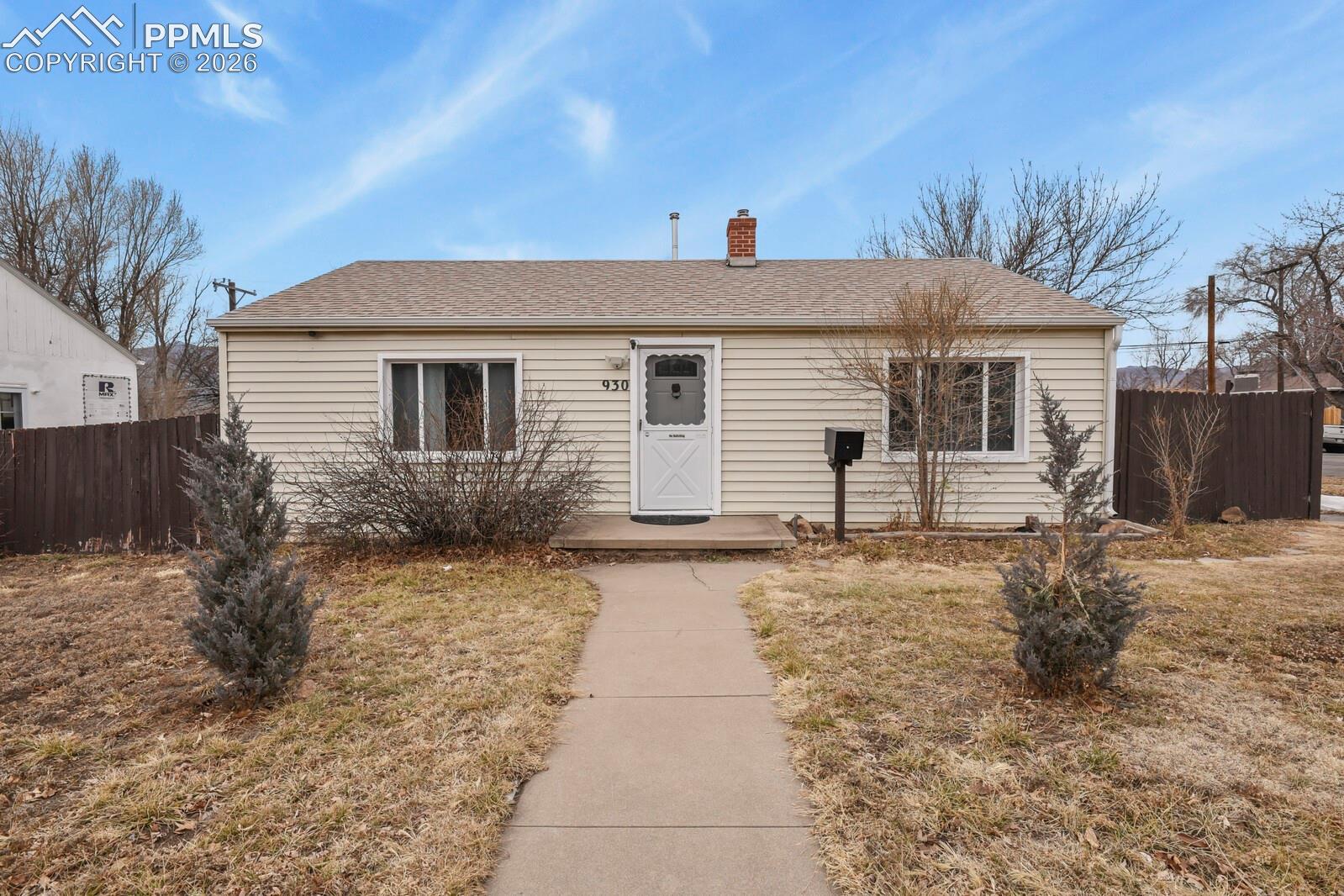 Single-story beige home with a white front door and concrete walkway through a dormant yard.