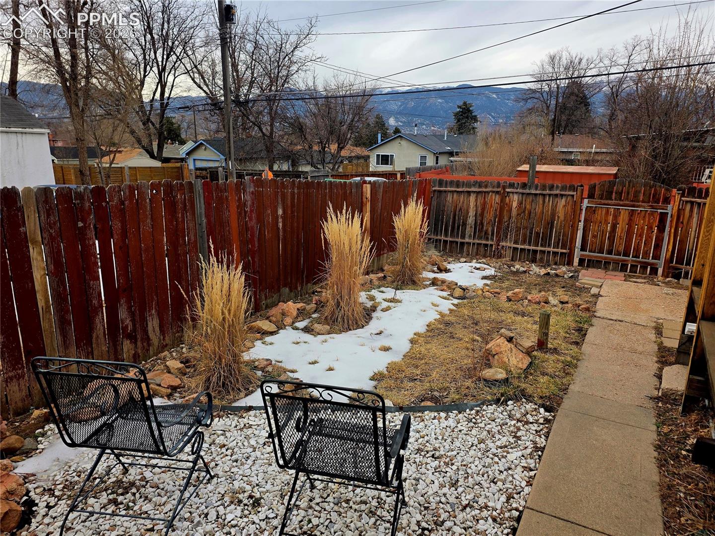 Backyard with a red privacy fence, gravel seating area, snow patches, and mountain views.