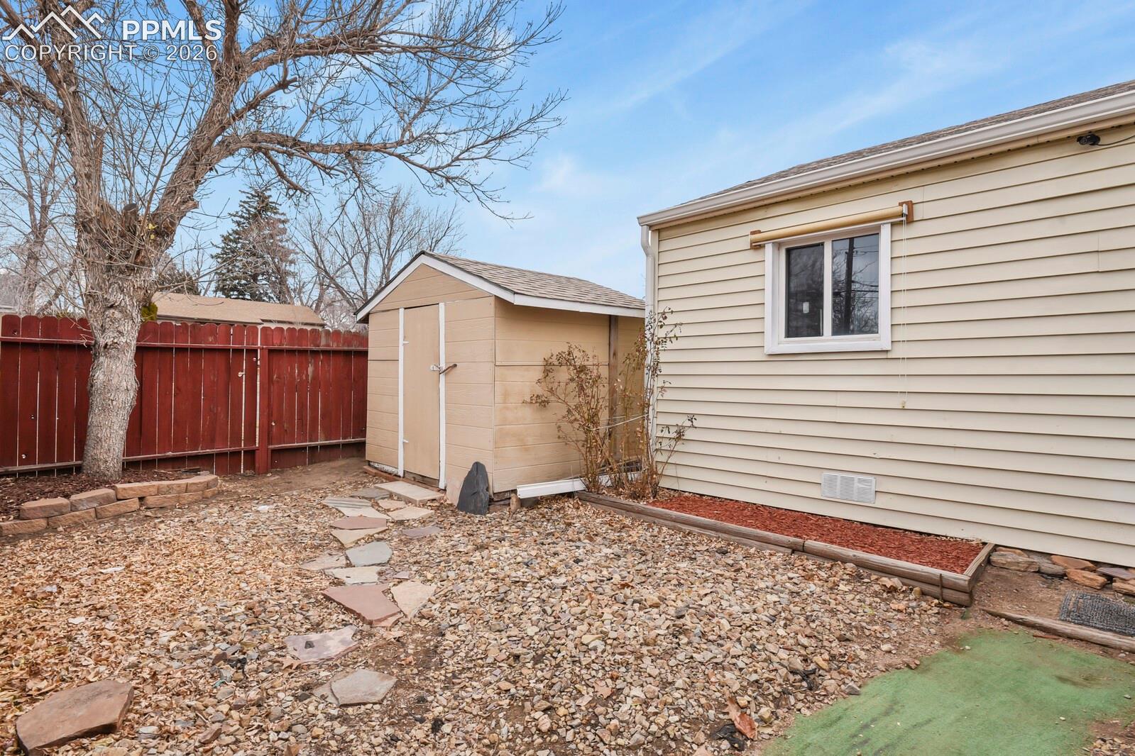 Backyard with a small storage shed, red privacy fence, and rock-covered ground with stepping stones.
