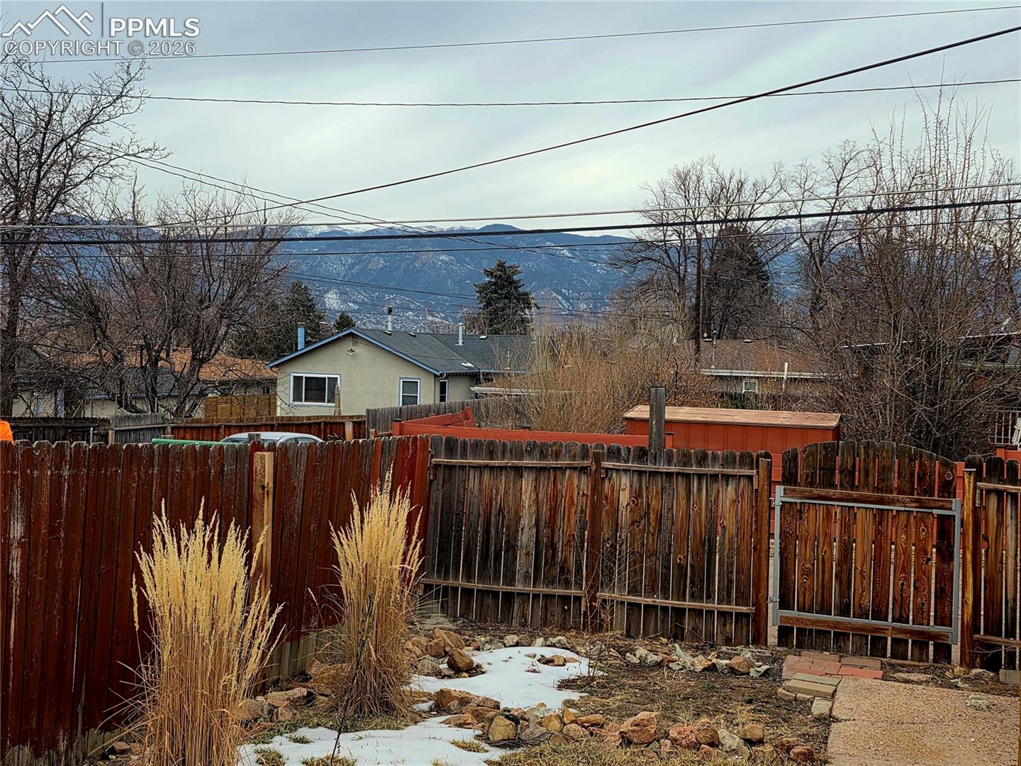 Fenced backyard with patches of snow and a view of mountains beyond neighboring homes.