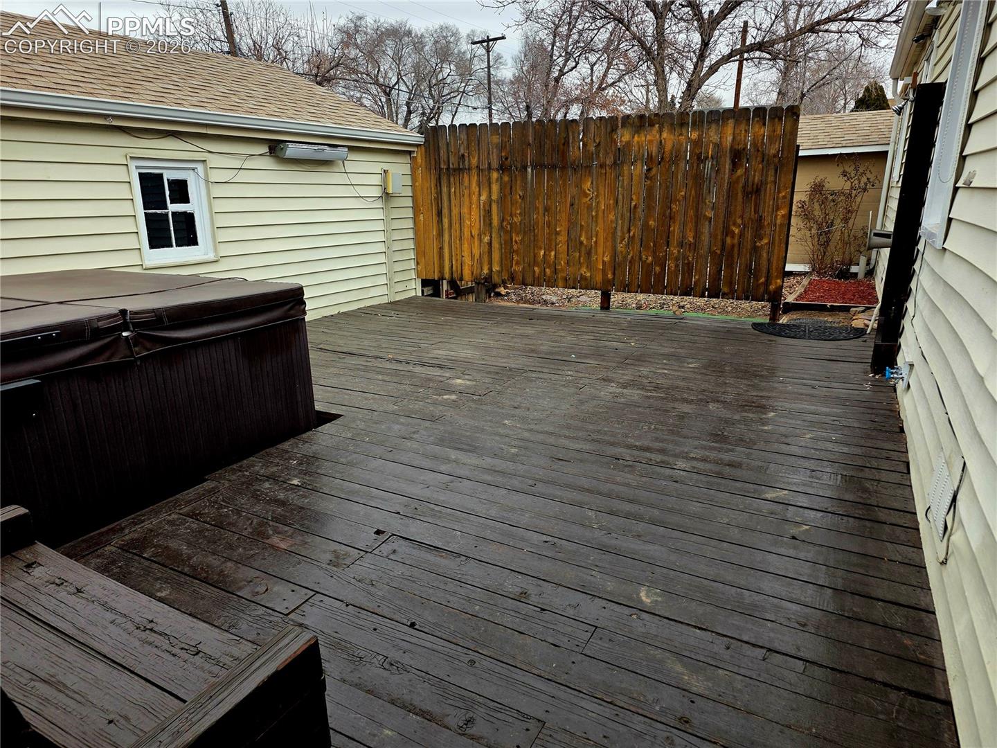 Wooden deck with a large hot tub and tall privacy fence.