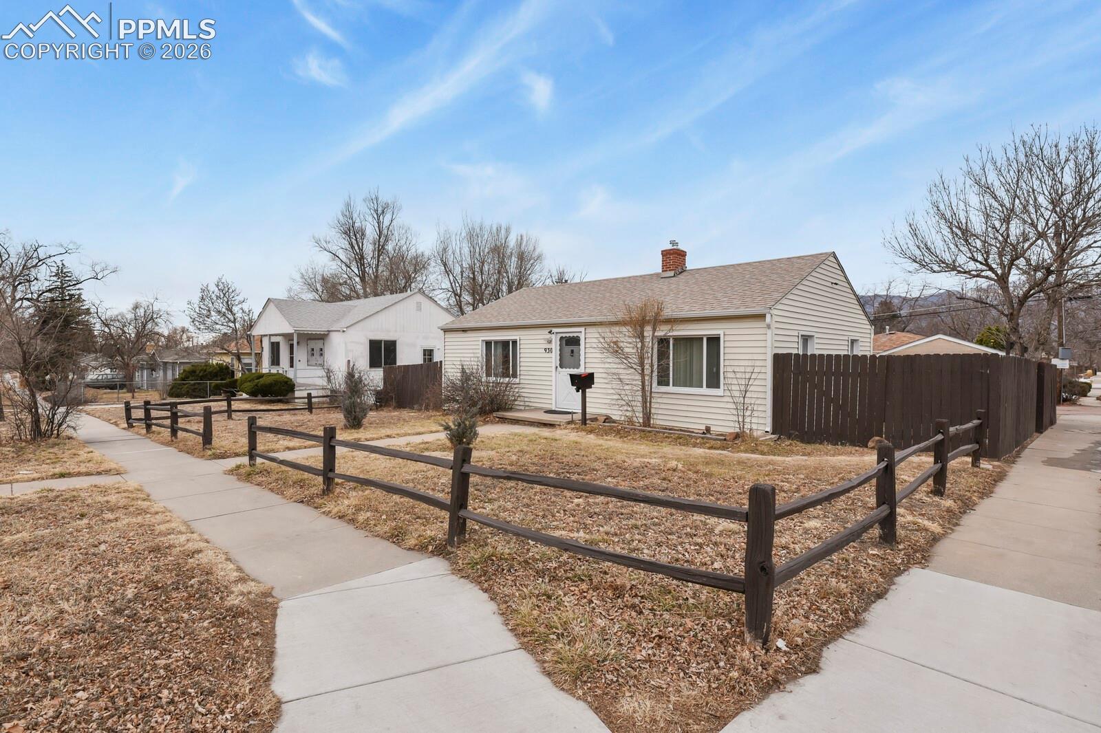 Single-story beige house with a fenced front yard and sidewalks.