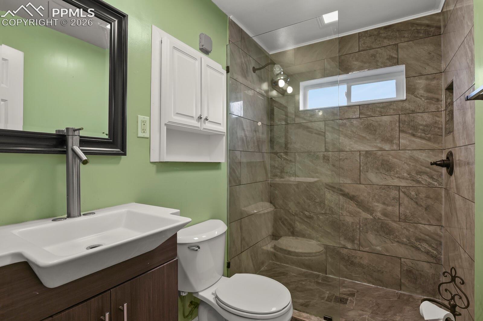 Bathroom with a glass-enclosed, brown-tiled shower, vessel sink, and green walls.