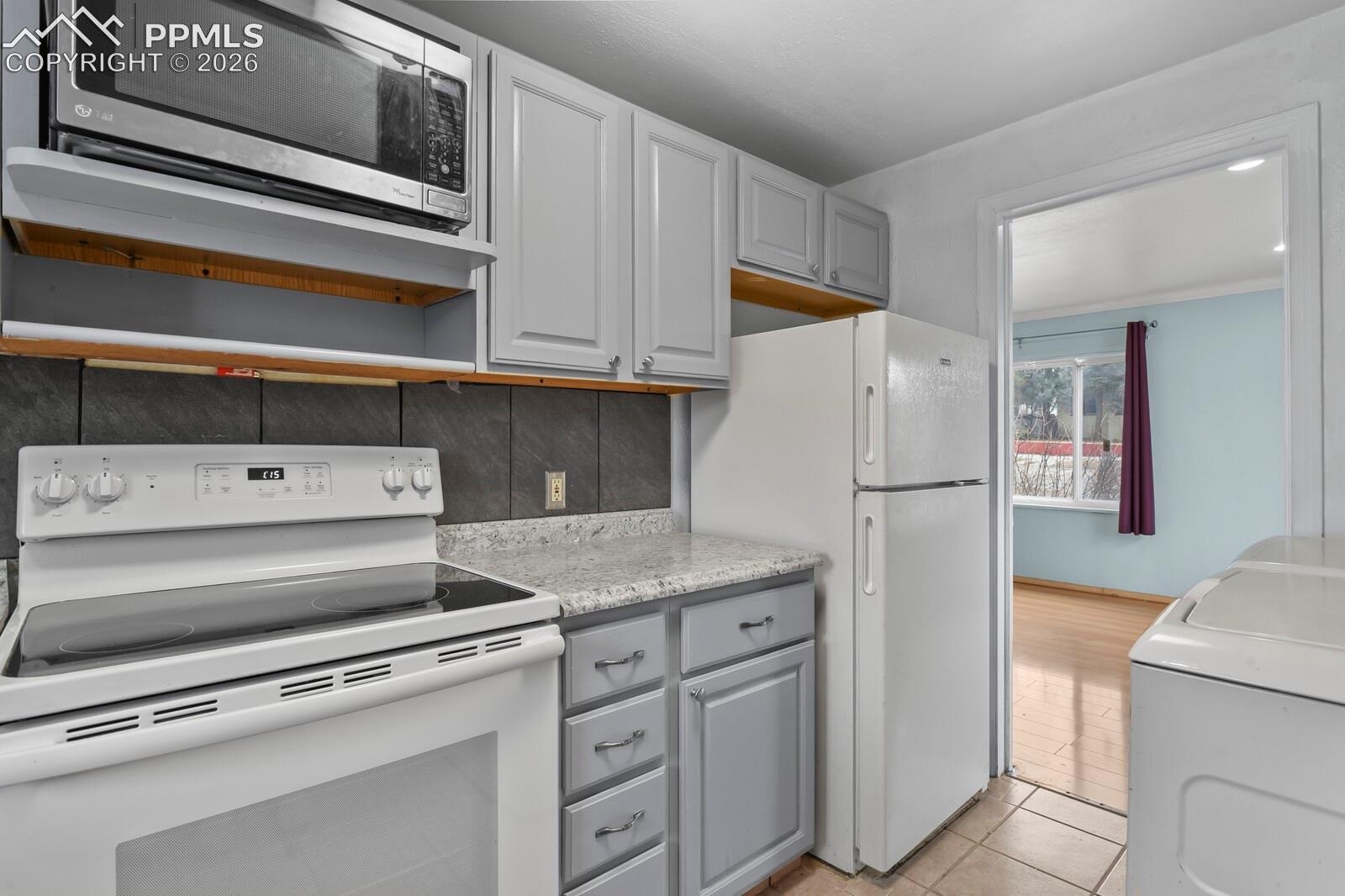 Kitchen with white cabinets, electric range, microwave, refrigerator, and a washer beside the doorway.