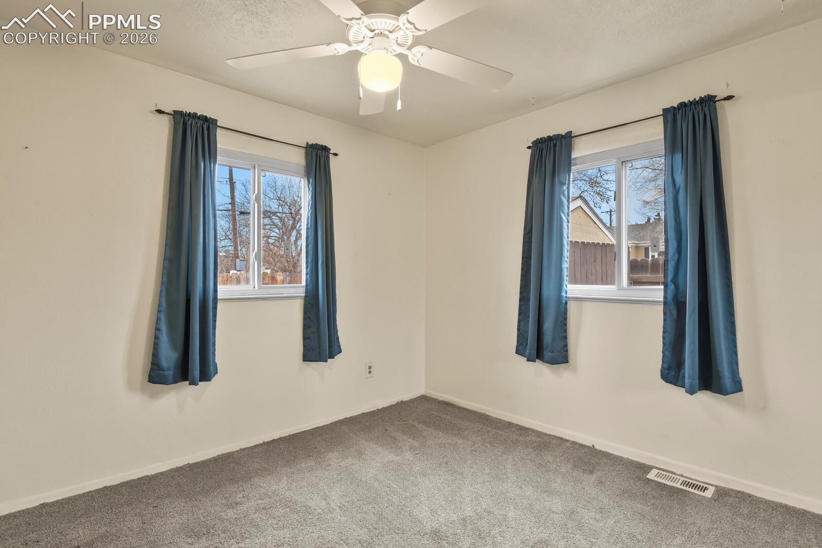 Empty bedroom with gray carpet, two curtained windows, and a ceiling fan.