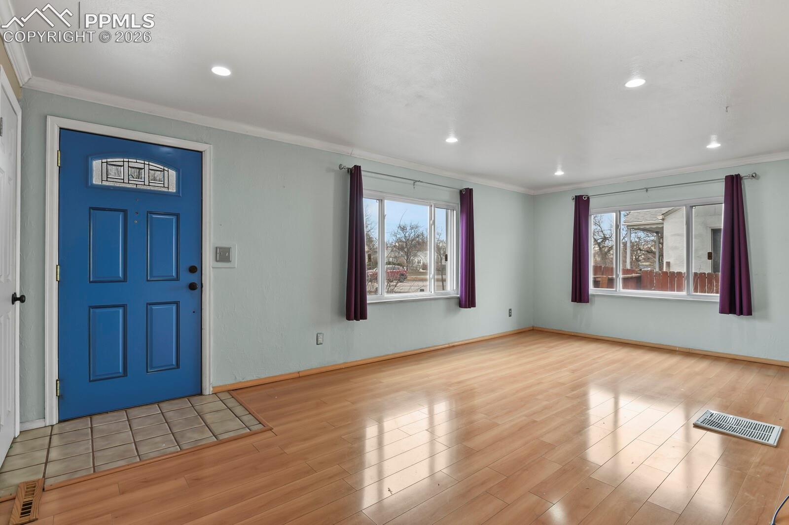 Vacant entry room with a blue front door, two curtained windows, and light wood flooring.