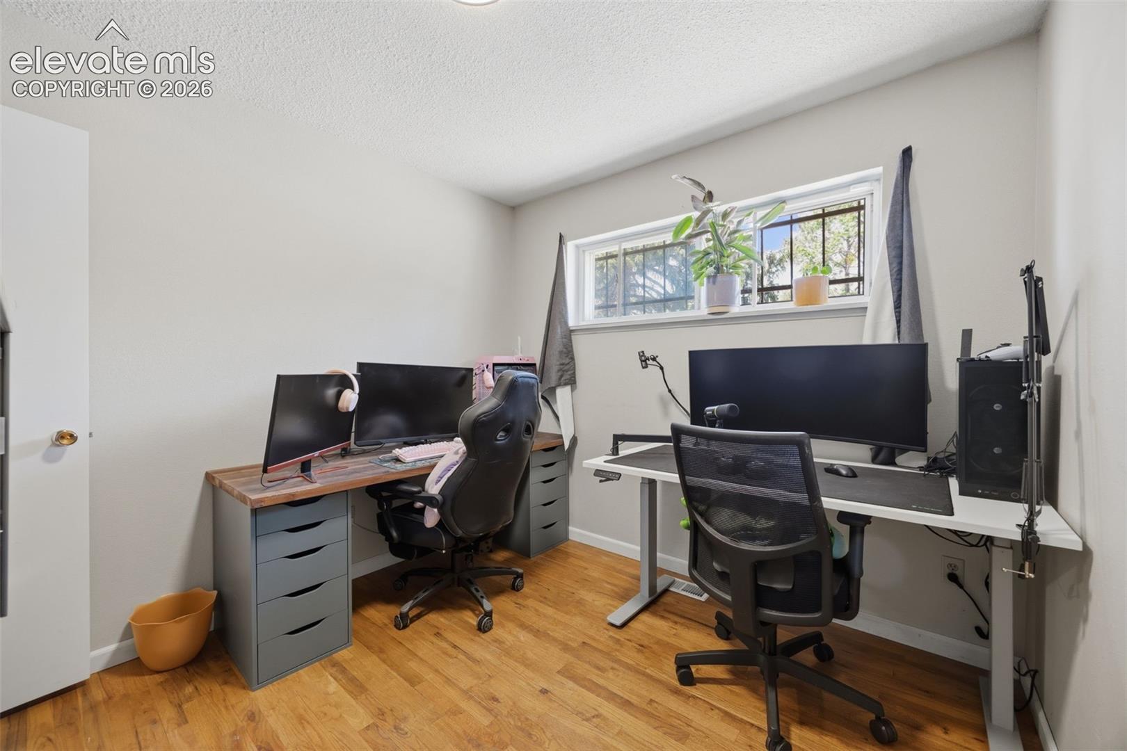 Home office with two computer workstations, ergonomic chairs, and a narrow window with plants.