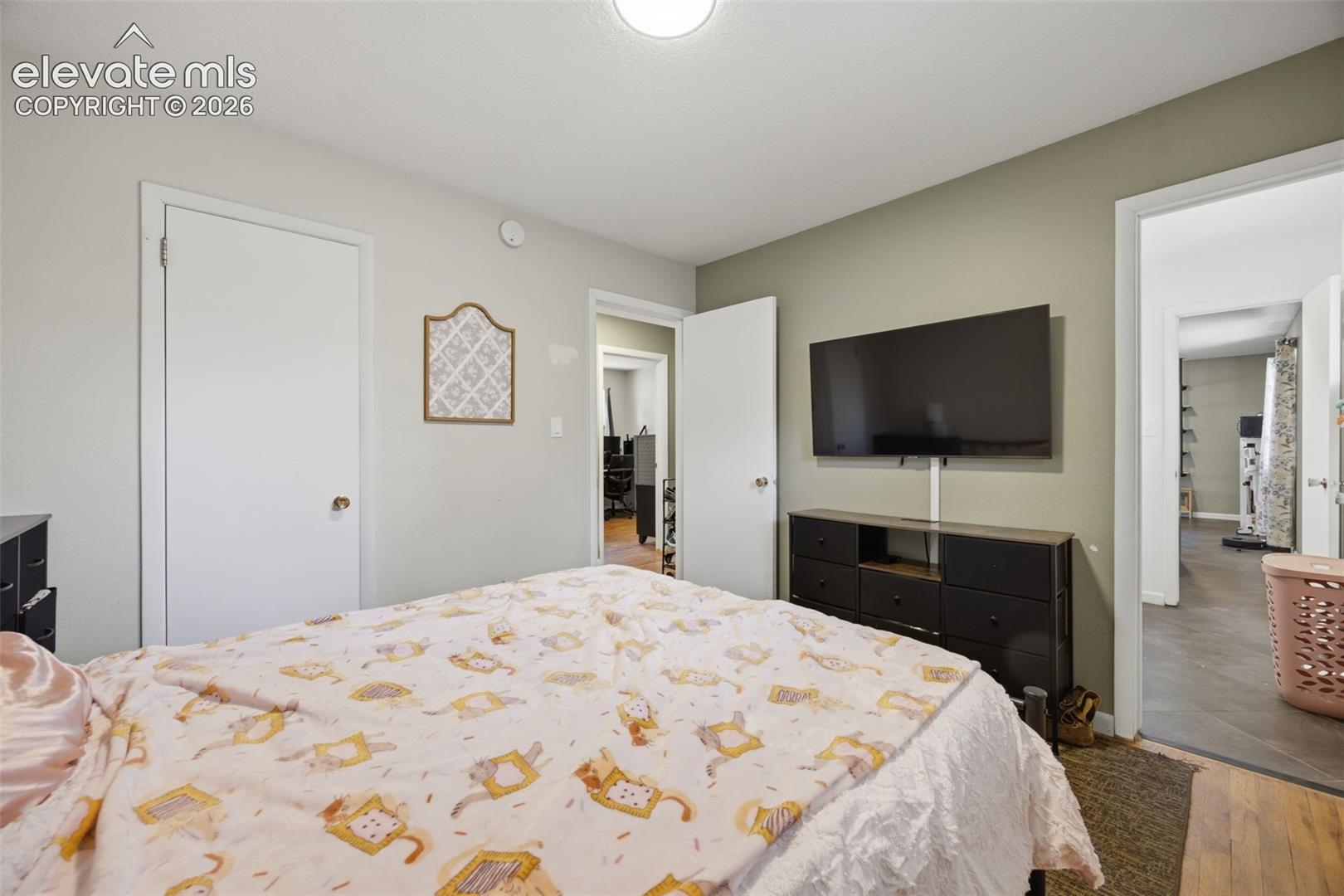 Bedroom with a cat-patterned bedspread, wall-mounted television, and dark dresser.
