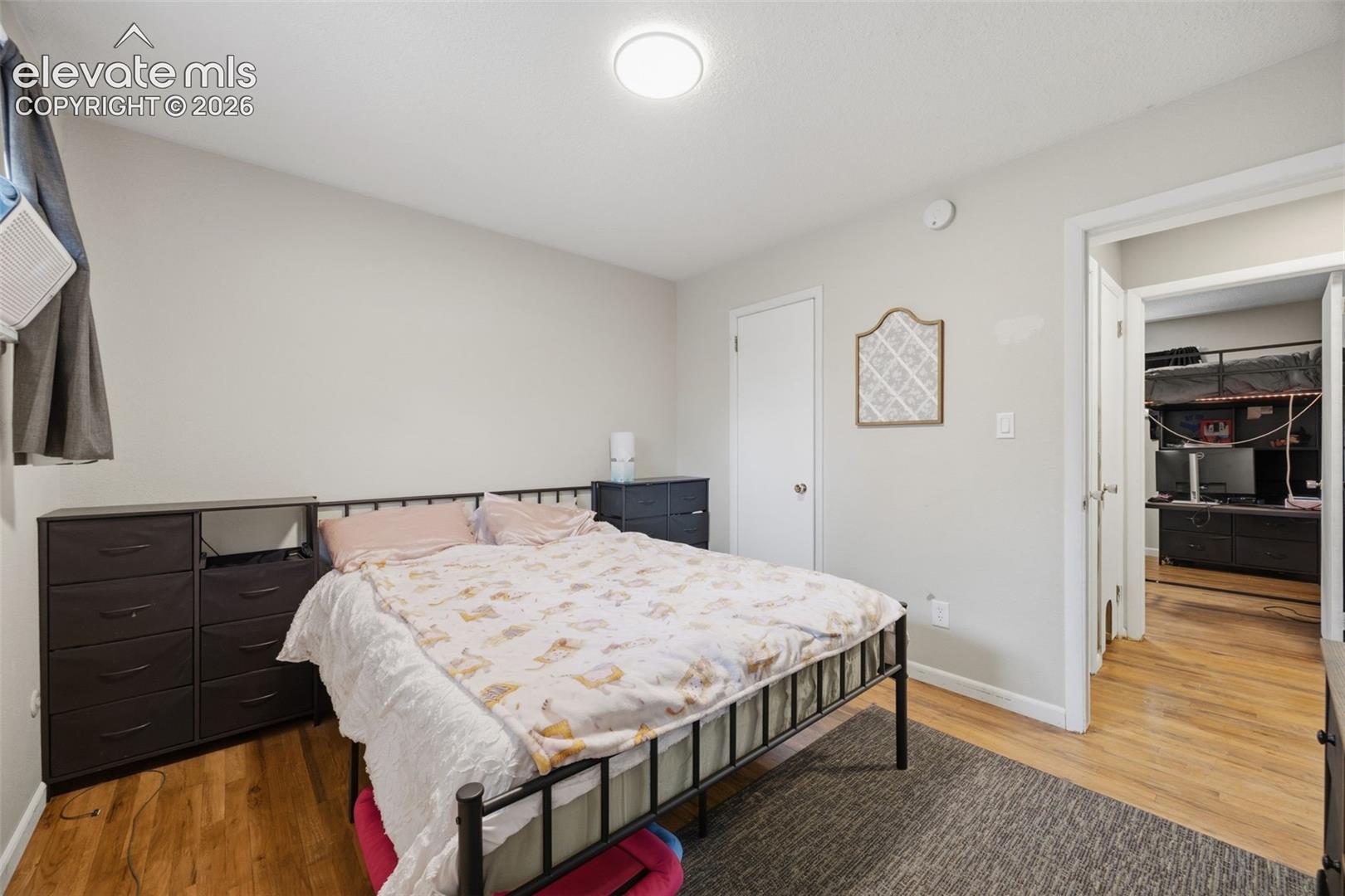 Bedroom with a black metal bed and patterned bedding, opening onto a room with a bunk bed and desk.