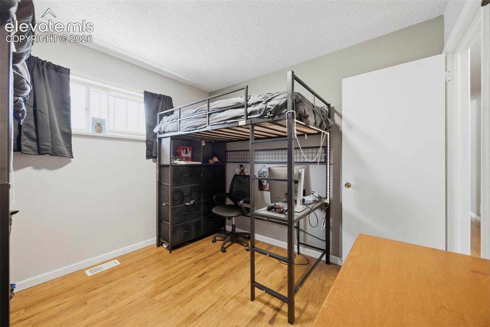 Bedroom with a lofted bed above a compact desk and computer workspace.