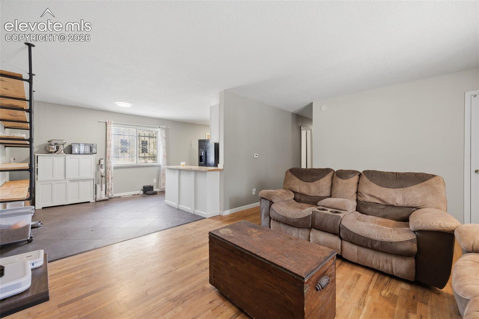 Living room with a brown reclining sofa, wooden chest coffee table, and open kitchen area.