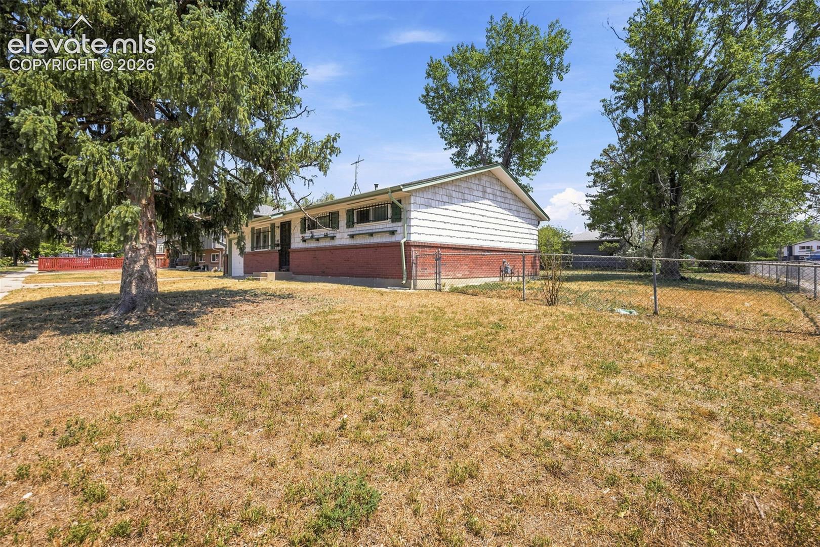 Single-story house with white siding, a red brick lower wall, and a fenced, dry lawn.
