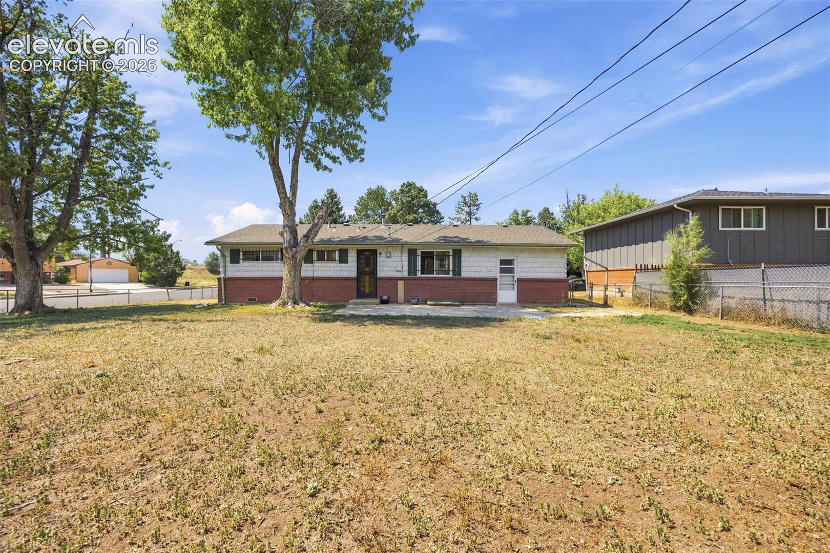 Single-story ranch house with white siding, red brick lower facade, green shutters, and a dry yard.