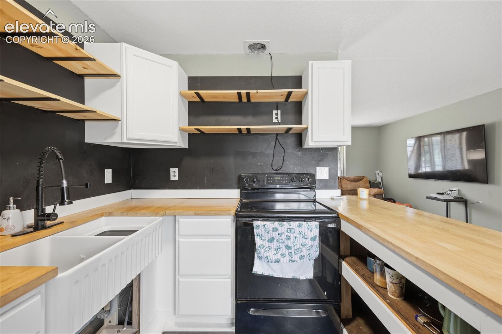 Kitchen with a farmhouse sink, black range, butcher-block counters, and open wood shelves.