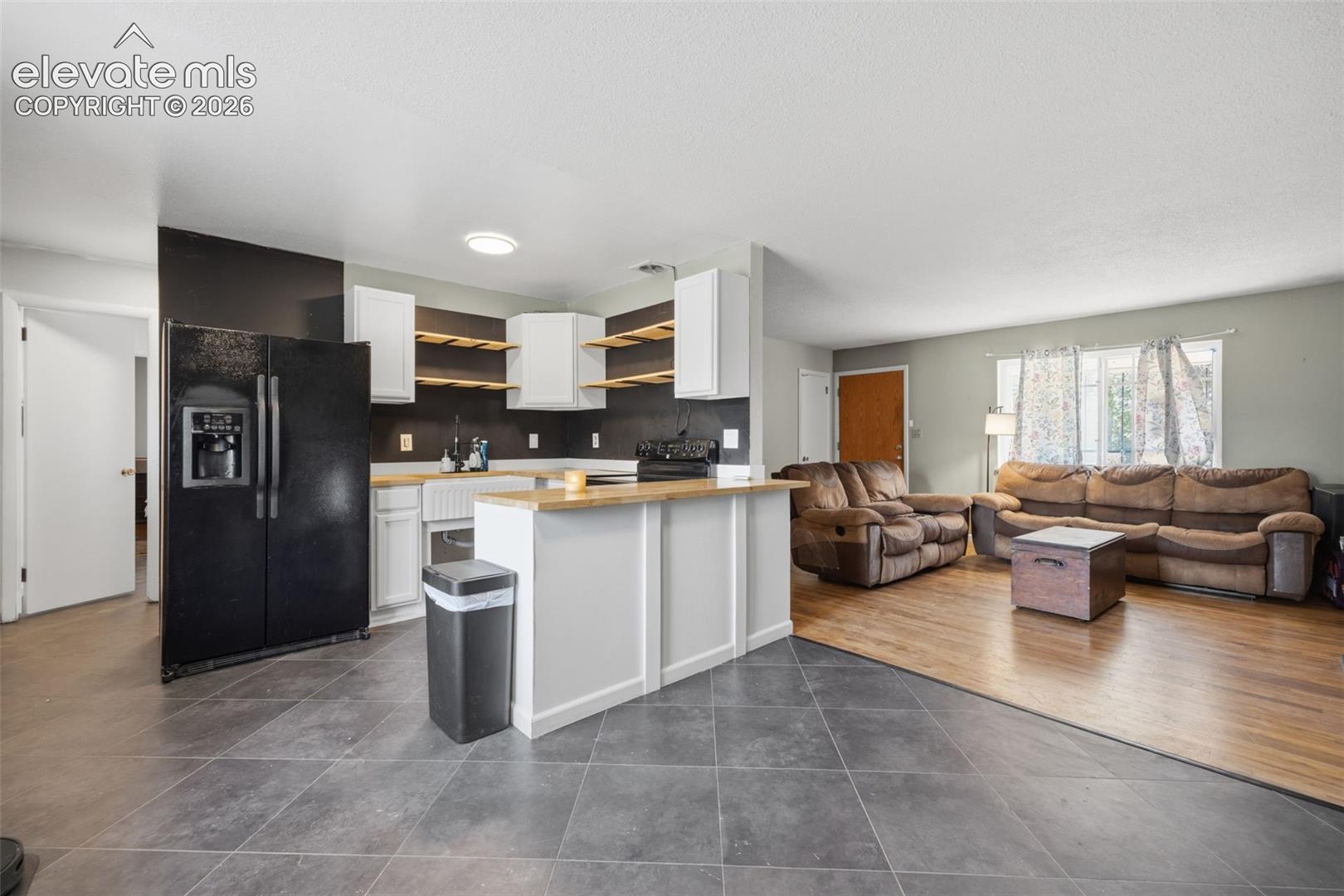 Kitchen and living room with a wood-counter peninsula, open shelves, brown sofas, and wood flooring.