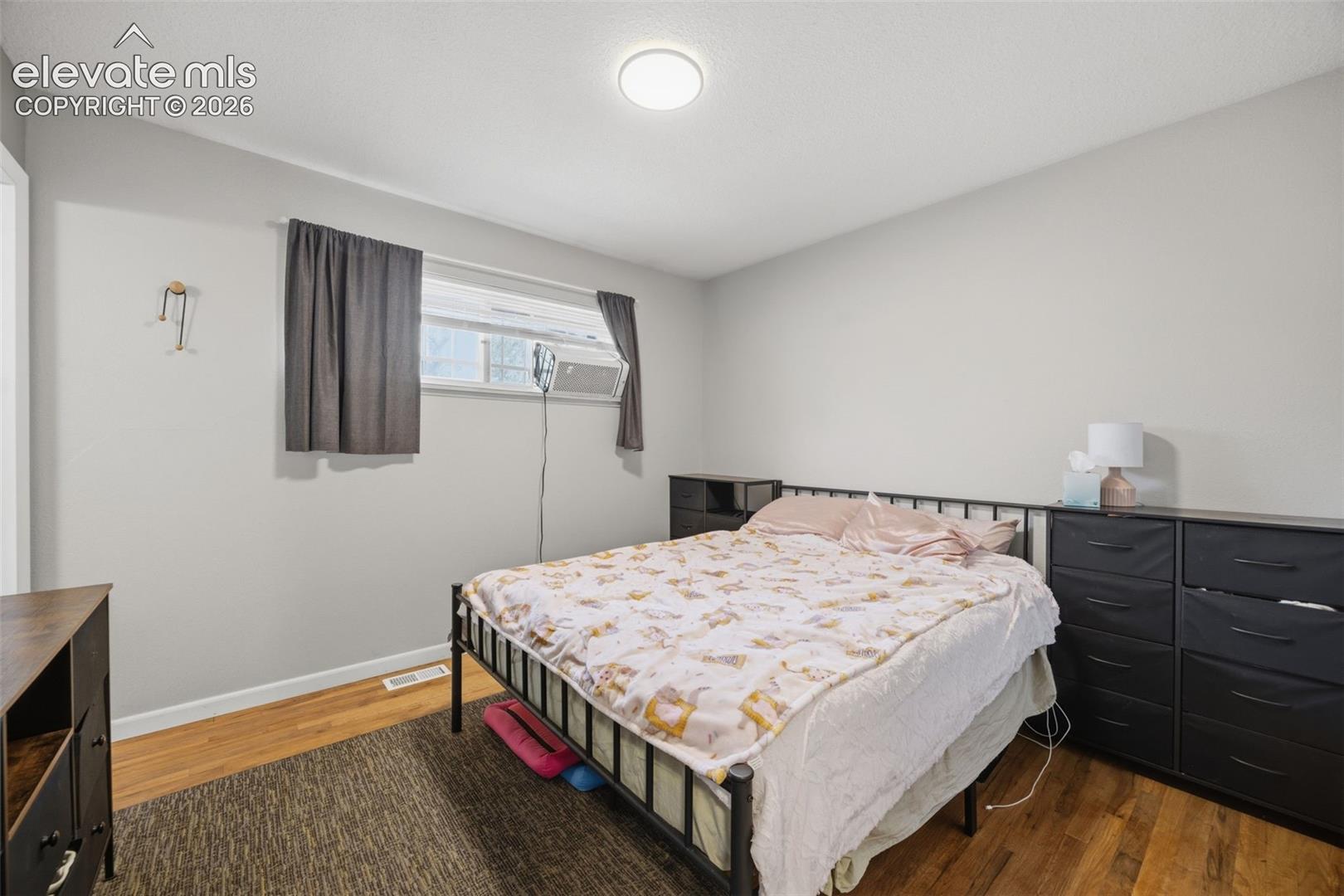 Bedroom with a black metal bed, patterned bedding, dark dressers, and a window air conditioner.