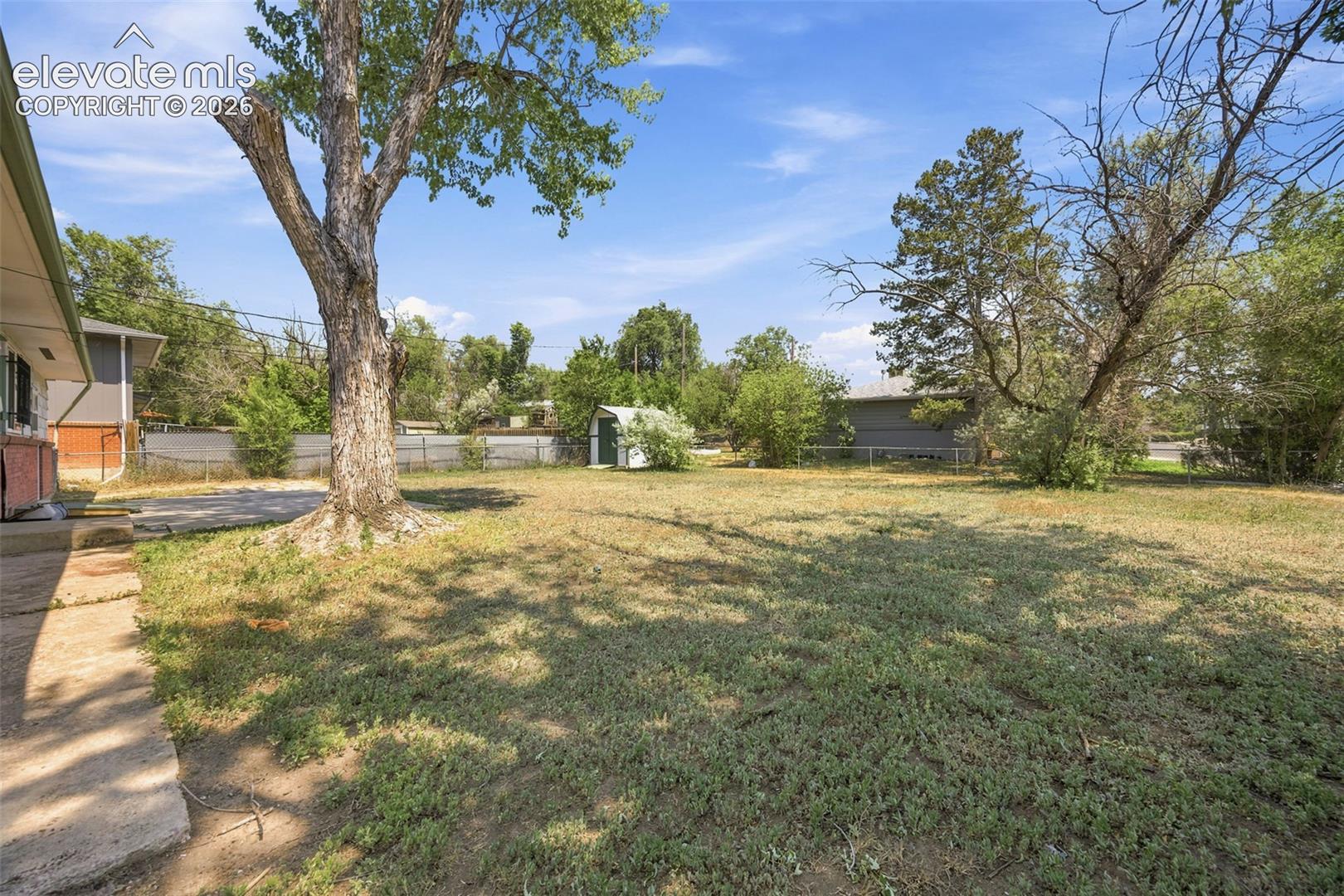Backyard with mature trees, patchy lawn, concrete patio, and a small detached shed.