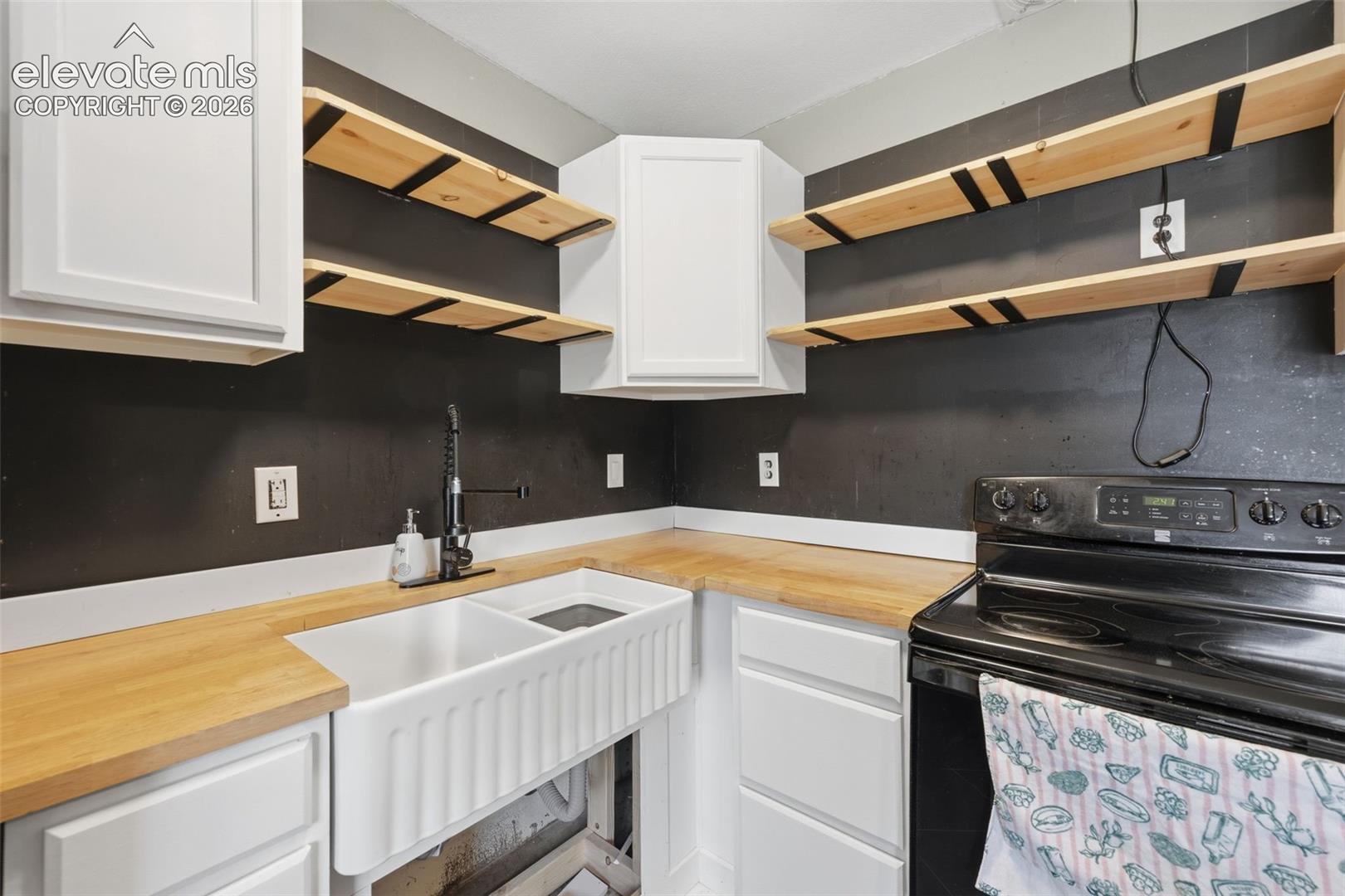Kitchen with a deep farmhouse sink, butcher-block counters, open shelves, and a black electric range.