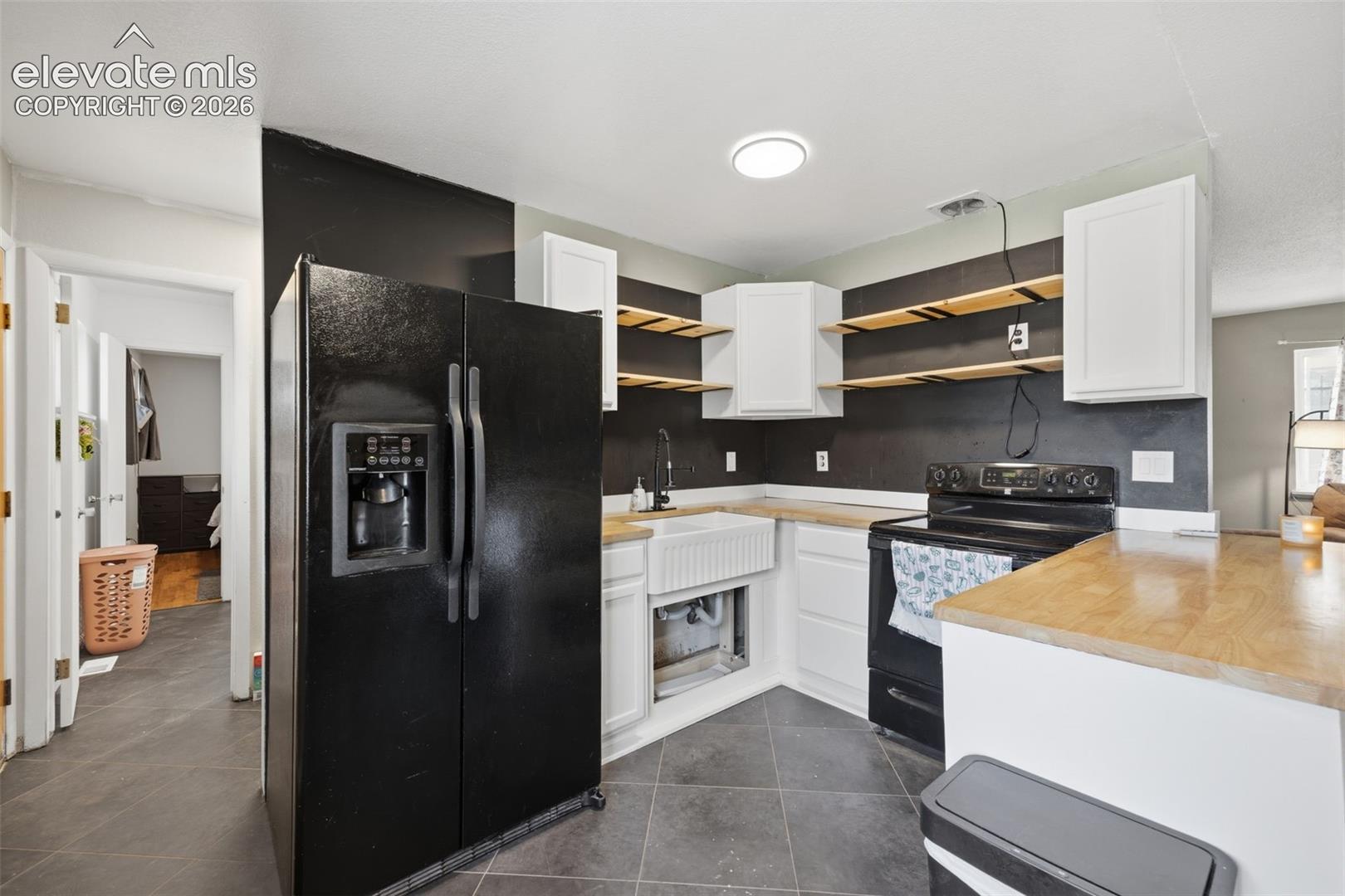 Kitchen with white cabinets, open wood shelves, dark backsplash, and a black refrigerator and range.