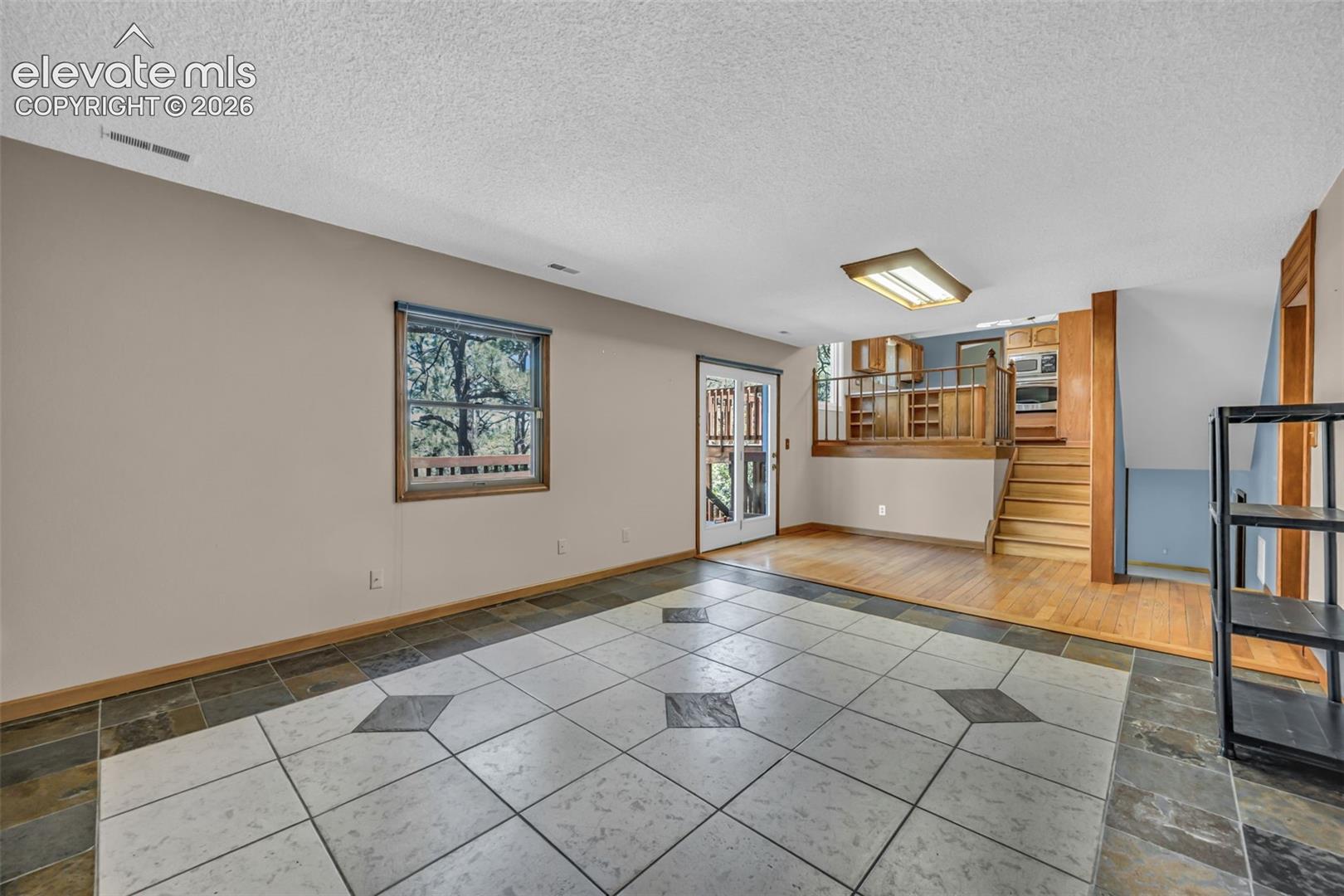 Open living area with patterned tile flooring, raised hardwood kitchen, and stairs.