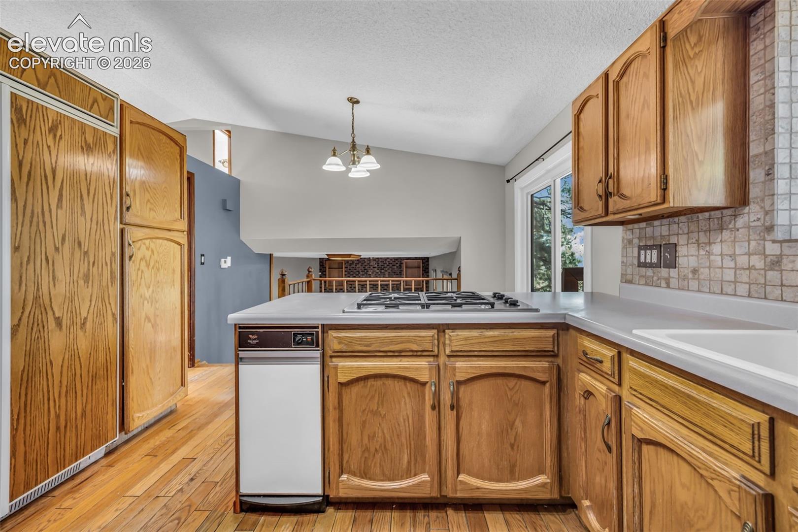 Kitchen with oak cabinets, hardwood floors, a central cooktop, and tiled backsplash.