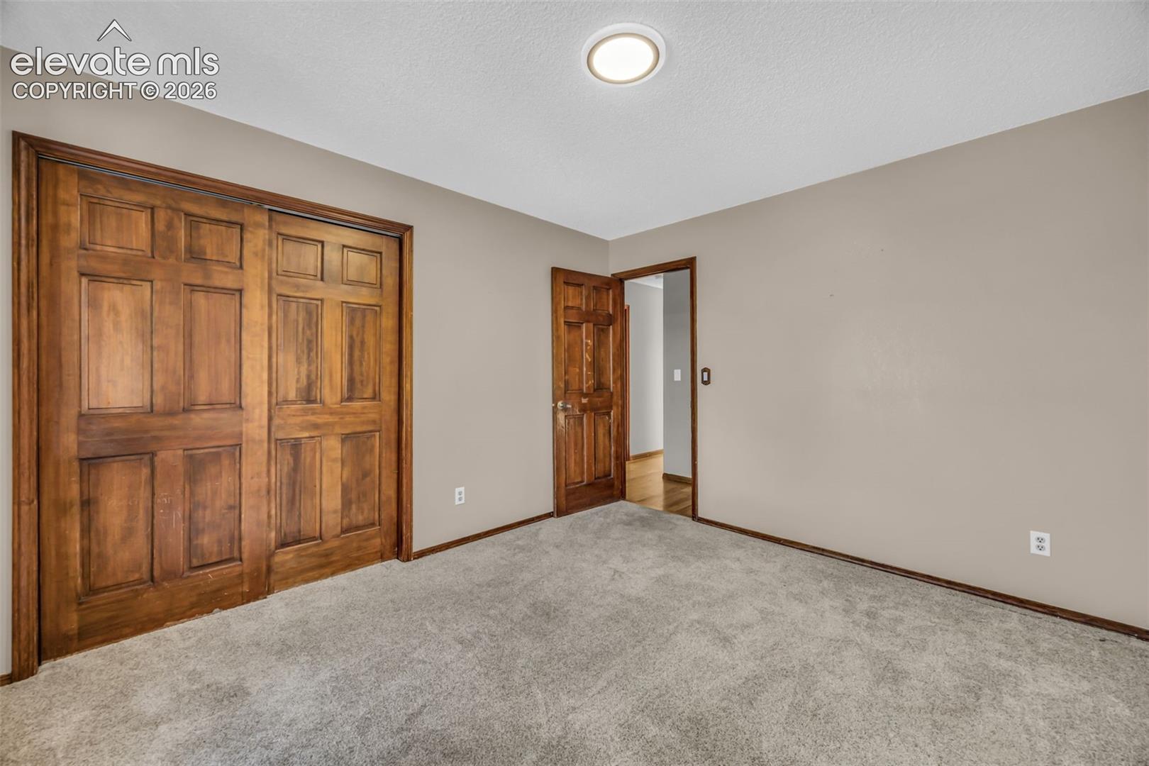 Empty carpeted bedroom with large wooden closet doors and an open doorway.