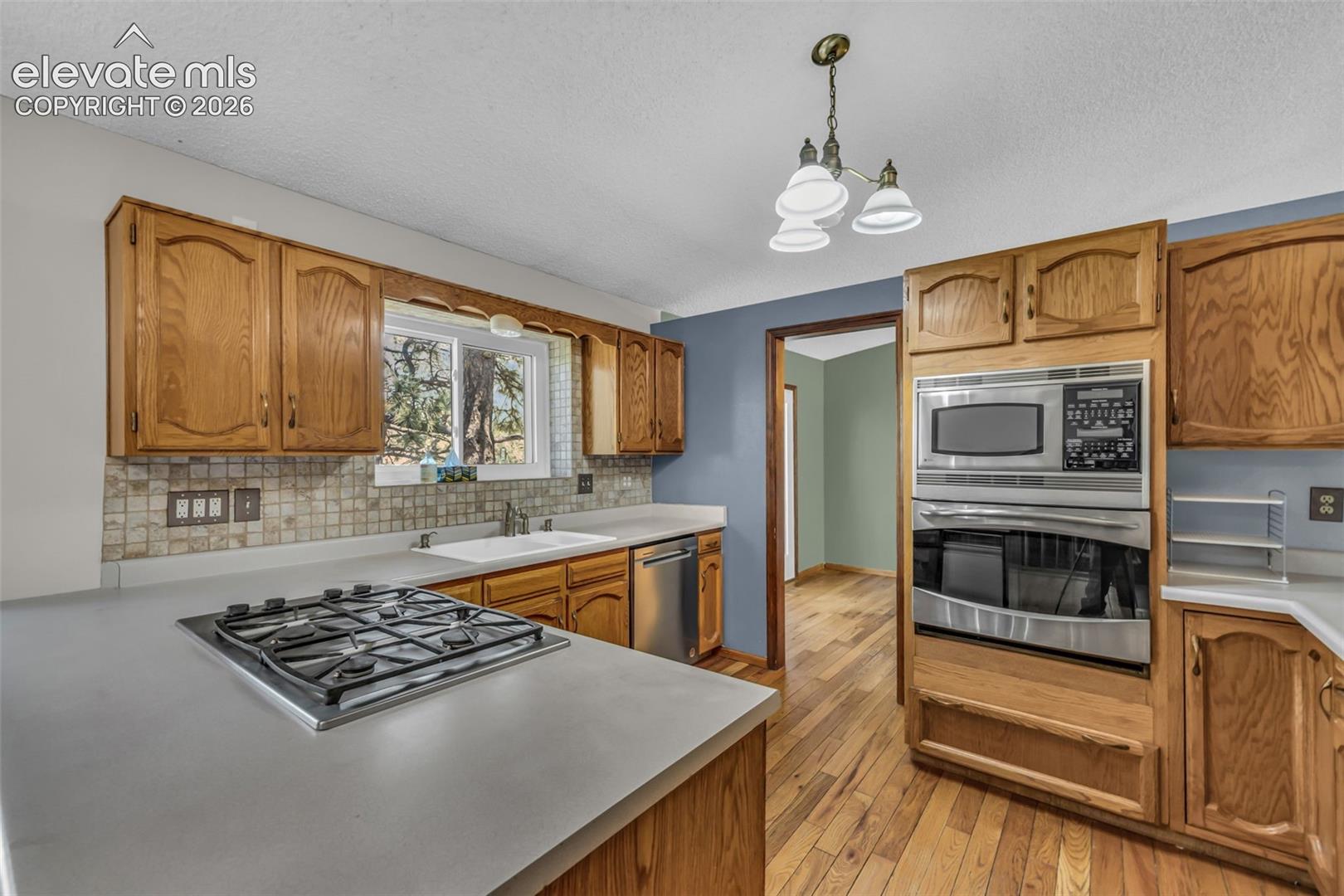 Kitchen with wood cabinets, tiled backsplash, gas cooktop, and built-in stainless steel oven.