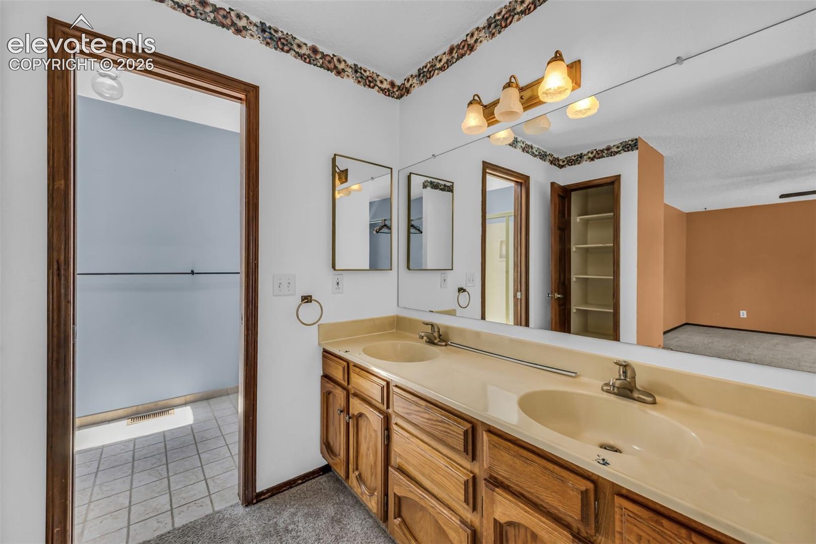 Bathroom with a long double-sink vanity, wall-length mirror, and tiled shower.