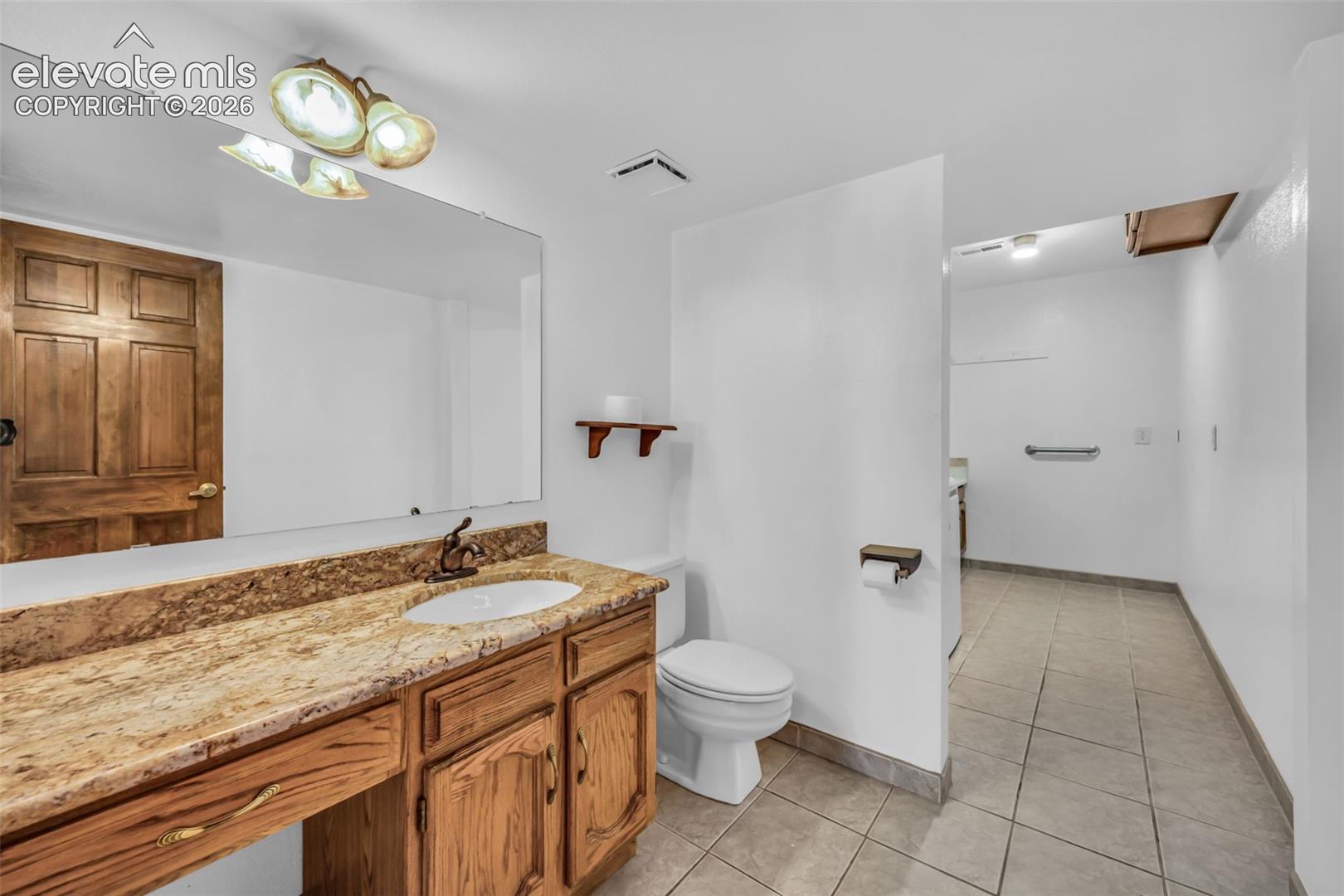 Bathroom with a wood vanity, granite countertop, toilet, and tiled shower area.