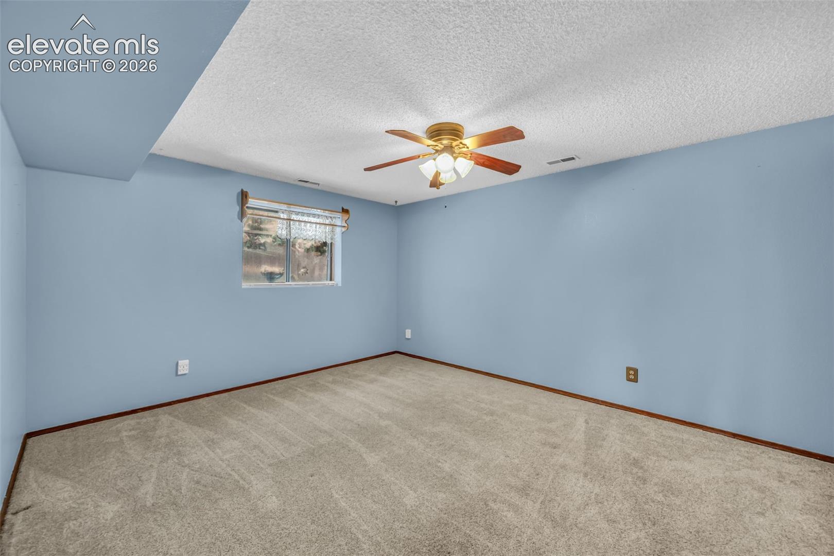 Vacant bedroom with blue walls, beige carpet, a small window, and ceiling fan.