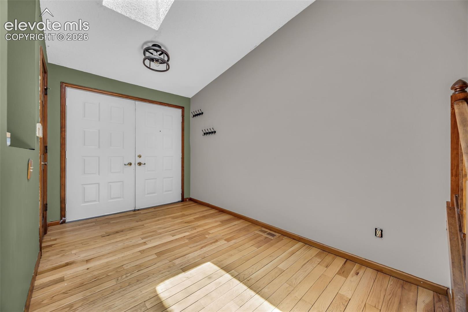 Entryway with white double doors, sage-green walls, and hardwood floors.