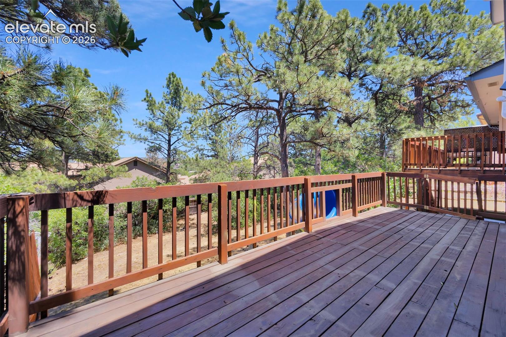 Wooden deck overlooking pine trees, with a raised section and railing.