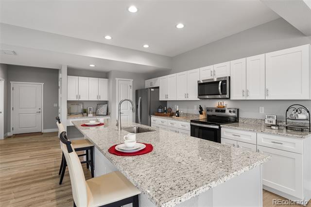 Modern kitchen with a large granite island, white cabinetry, and stainless steel appliances.