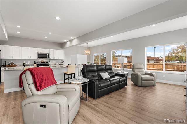 Open-plan living room with black leather sofa, pale recliners, and large windows overlooking a fenced yard.