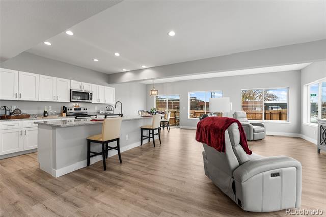 Open-plan kitchen and living room with a large island, light wood floors, and a gray recliner draped with a red blanket.