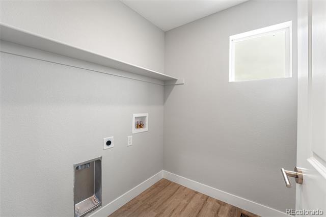 Empty laundry room with a long wall shelf, small high window, and wood-look floor.