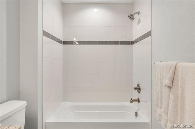 White bathtub and shower with tiled walls, chrome fixtures, and white towels.